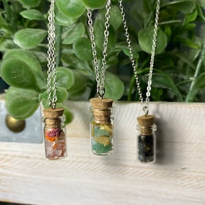 May include: Three silver chain necklaces with small glass bottles filled with different colored crystals. The bottles are corked and hang from the chains.