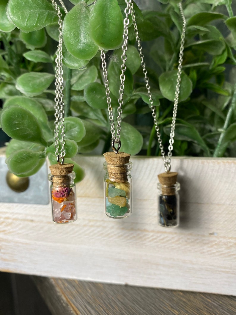 May include: Three silver chain necklaces with small glass bottles filled with different colored crystals. The bottles are corked and hang from the chains.