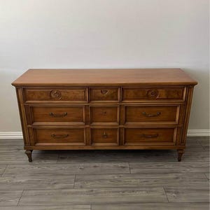 May include: A wooden dresser with nine drawers and a light brown finish. The dresser has decorative ring pulls and is set on short, tapered legs. The top of the dresser is flat and smooth. The dresser is a classic piece of furniture.