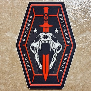May include: A black and red patch featuring a skull and a sword design. The patch includes the words "KONNI" and "ВОЕННАЯ ОПЕРАЦИЯ" in white text. Two white stars are also visible.