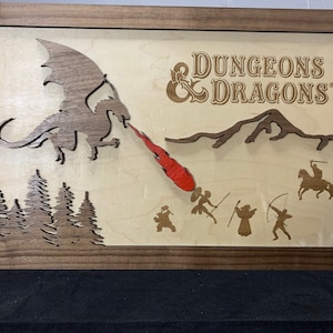 May include: Wooden framed artwork featuring a dragon breathing fire at a group of figures, with the text "DUNGEONS & DRAGONS". The artwork has a layered design with a dark brown frame and accents, and a light wood background.