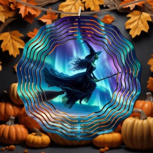 May include: A decorative Halloween-themed wind spinner featuring a witch on a broomstick against a backdrop of aurora borealis. The spinner has a layered design with blue, purple, and gold accents. Pumpkins and fall leaves surround the spinner.