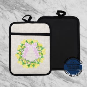 May include: Two pot holders. One is off-white with a black border and a lemon wreath design with a pink bow. The other is solid black. Both have a black loop for hanging. The pot holder with the design has the text "Wild Outdoor Creations®" on it.
