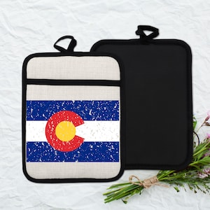 May include: Two pot holders. One features the Colorado state flag with a distressed design. The flag has blue stripes, a white stripe, and a red circle with a yellow center. The other pot holder is solid black.