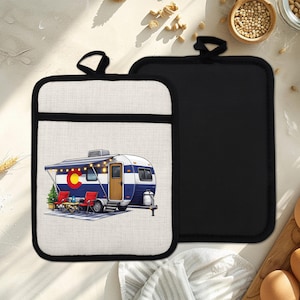 May include: Two pot holders. One is black, the other is off-white with a black border and a graphic of a blue and white camper with a Colorado flag on the side. The camper has a door, awning, and string lights.