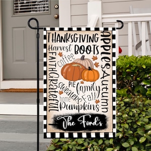 Könnte beinhalten: Eine rechteckige Gartenflagge mit einem schwarz-weiß karierten Rand. Die Flagge zeigt die Wörter "Thanksgiving", "Harvest", "Boots", "Pumpkins" und "Family". Drei Kürbisse befinden sich in der Mitte. Der Text "The Ford's" steht unten.