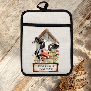May include: A white and black oven mitt with a black border and a black hanging loop. The mitt features a cartoon cow graphic with the text "I'M HAVING A GOOD DAY. LET'S NOT RUIN IT!"