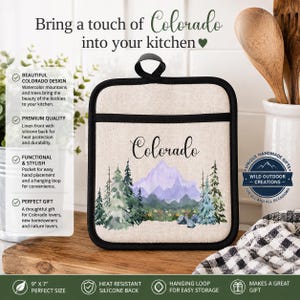 May include: A square pot holder with a black trim and a hanging loop. The front features a beige fabric with a watercolor illustration of purple mountains, green pine trees, and wildflowers. The word Colorado is printed in black script above the art.