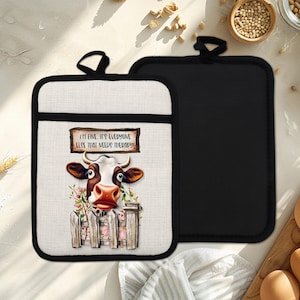 May include: Two pot holders. One features a cow graphic with the text "I'M FINE. IT'S EVERYONE ELSE THAT NEEDS THERAPY!". The other is solid black. Both have a black trim and a loop for hanging.