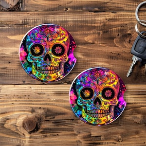Könnte beinhalten: Zwei Auto-Untersetzer mit einem farbenfrohen Totenkopf-Design. Die Totenköpfe sind mit Blumen und leuchtenden Farben wie Pink, Gelb, Blau und Grün verziert. Im Hintergrund sind Autoschlüssel zu sehen.
