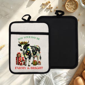 May include: A pair of pot holders with a black and white cow graphic. The cow is decorated with Christmas lights and a wreath, standing in front of wrapped gifts. The text reads "MAY YOUR DAY BE FARMY & BRIGHT."