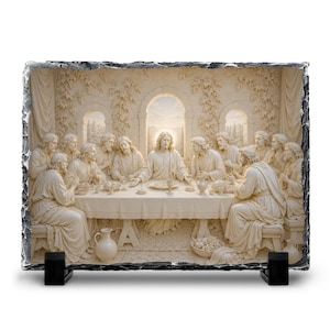 May include: A rectangular, off-white relief sculpture depicting the Last Supper. The scene features figures seated around a table, with architectural details in the background. The sculpture is mounted on a black stand.
