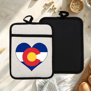 May include: Two pot holders. One has a heart-shaped design with the Colorado state flag in blue, white, red, and yellow. The other is plain black. Both have a black hanging loop and a black border.