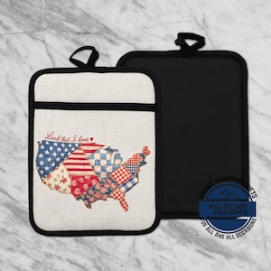 May include: A white and black pot holder with a stitched map of the United States, featuring patchwork patterns in red, white, and blue. The text "Land that I love" is written in red script. A black pot holder is next to it.