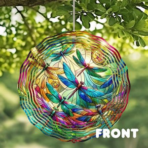 May include: A colorful, round wind spinner featuring a stained-glass design of dragonflies. The dragonflies are in shades of blue, green, and orange, set against a yellow background. The word "FRONT" is visible at the bottom. The spinner is hanging from a tree branch.