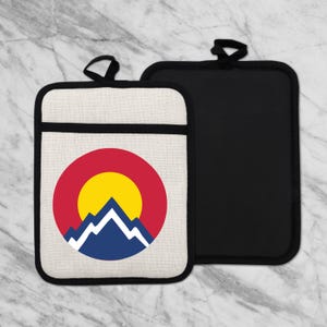 May include: Two pot holders. One is off-white with a black border and a Colorado state flag design. The other is solid black. Both have a loop for hanging. The Colorado flag design features a red circle, yellow sun, and blue and white mountains.