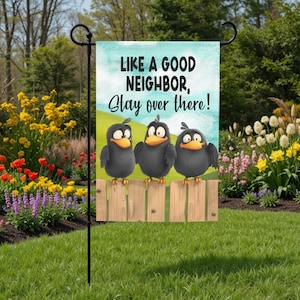 May include: A garden flag with the text "LIKE A GOOD NEIGHBOR, Stay over there!" features three cartoon crows perched on a wooden fence. The flag has a light blue and green background, and is displayed in a garden setting.