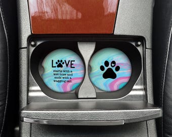 Puede incluir: Dos posavasos redondos para coche con un diseño de remolino colorido. Un posavasos presenta una huella de pata con un corazón y el texto "LOVE starts with a wet nose and ends with a wagging tail."