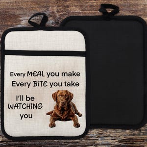 Könnte beinhalten: Ein weißer Baumwoll-Topflappen mit schwarzem Besatz zeigt einen braunen Labrador Retriever Hund und den Text "Every MEAL you make Every BITE you take I'll be WATCHING you".