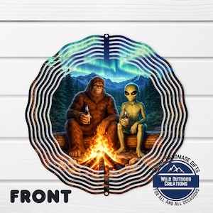 Pode incluir: Uma placa de metal redonda com um Bigfoot e um alienígena sentados perto de uma fogueira, cada um segurando uma garrafa. O fundo mostra uma floresta, montanhas e uma aurora boreal. A placa tem uma borda decorativa e a palavra "FRONT".