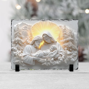 May include: A white relief sculpture of the Holy Family, featuring Mary, Joseph, and baby Jesus, set against a backdrop of stylized trees and a radiant light. The artwork is mounted on a rectangular slate base with black supports.