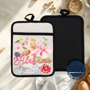 May include: Two pot holders. One features a design with the word "Alabama" in script, a football, flowers, and a bird. The other is solid black. Both have a black loop for hanging.