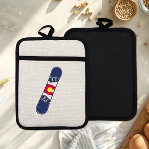 May include: Two rectangular pot holders. One is off-white with a black border and a blue snowboard graphic with the Colorado state flag. The other is solid black with a black loop for hanging.