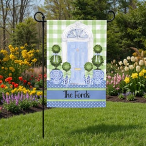 May include: A garden flag with a blue door design, topiary, and blue and white vases. The flag has a green and white checked background and a blue banner with the name "The Fords".