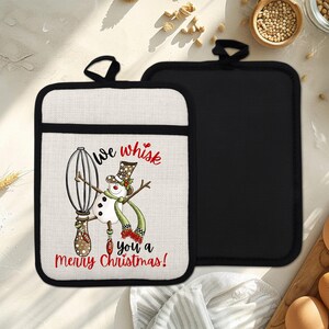 Puede incluir: Dos agarraderas navideñas. Una presenta un muñeco de nieve sosteniendo un batidor con el texto "we whisk you a Merry Christmas!". La otra es de color negro liso. Ambas tienen un ribete negro y un lazo para colgar.