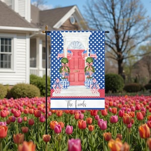 May include: A garden flag with a red door design, American flags, and a blue star-patterned background. The flag displays the text "The Lords" on a white banner. The flag is set in a garden of colourful tulips.