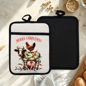 Puede incluir: Dos agarraderas navideñas. Una presenta una vaca, un cerdo y una gallina decorados con luces navideñas, con el texto "MERRY CHRISTMAS". La otra es de color negro liso. Ambas tienen un borde negro y un lazo para colgar.