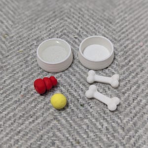 May include: Two white dog bowls, two white dog bones, a red and white rubber dog toy, and a yellow rubber ball.