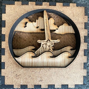 May include: A wooden box with a cutout design of a sword in the water. The sword is made of wood and has a detailed handle. The water is represented by waves and the background is a textured wood.