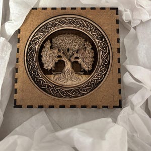 May include: A wooden wall art piece featuring a detailed Celtic knot design surrounding a tree of life with intricate branches. The piece is brown and has a rustic look.