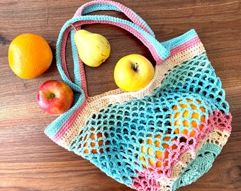 Può includere: Una borsa tote all'uncinetto multicolore piena di arance, mele e una pera. La borsa presenta un design a rete nei toni del blu, rosa e beige, con manici abbinati. La frutta è disposta su una superficie di legno.
