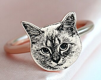May include: A rose gold ring with a black and white engraved image of a cat's face.