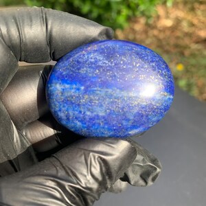 May include: A smooth, oval-shaped polished lapis lazuli stone with a deep blue color and flecks of gold pyrite.