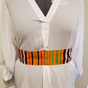 May include: A white long-sleeved blouse with a V-neck and a colorful patterned belt. The belt has stripes of orange, yellow, green, red, blue, and white.