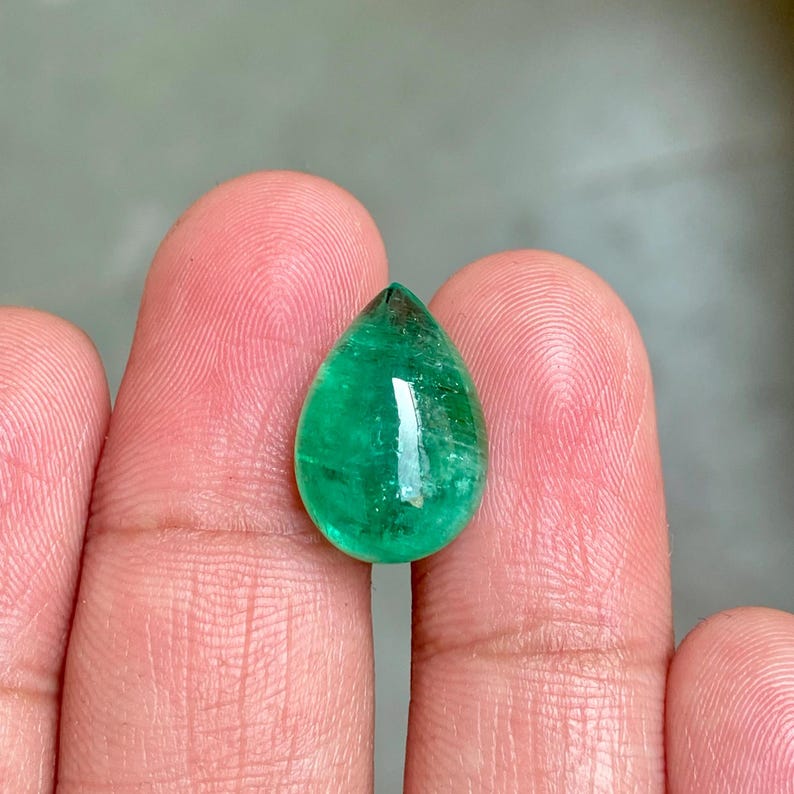 May include: A teardrop-shaped emerald gemstone with a deep green colour. The gemstone is faceted and has a high polish.