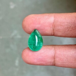 May include: A pear-shaped emerald gemstone with a deep green colour. The gemstone is cut and polished, and it has a smooth, glossy surface.