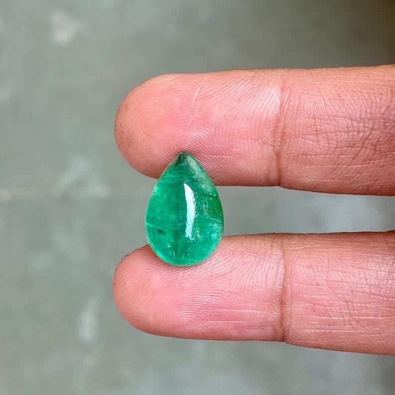 May include: A pear-shaped emerald gemstone with a deep green colour. The gemstone is cut and polished, and it has a smooth, glossy surface.