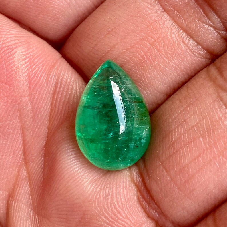 May include: A vibrant green emerald gemstone cut in a teardrop shape. The gemstone is faceted and has a high polish.
