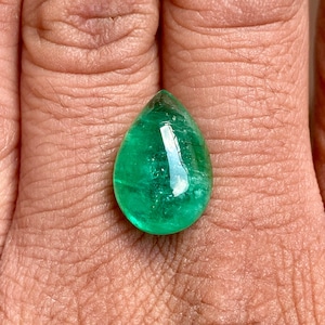 May include: A teardrop-shaped emerald gemstone with a deep green colour and a polished, faceted surface.