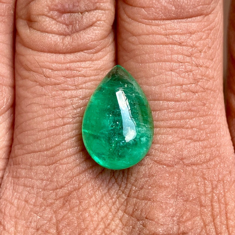 May include: A teardrop-shaped emerald gemstone with a deep green colour and a polished, faceted surface.