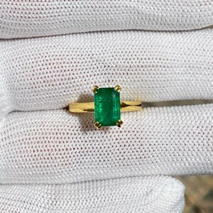 Puede incluir: Un anillo de oro con una gran piedra preciosa verde esmeralda engastada en forma cuadrada.