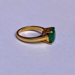 May include: A gold ring with a large, oval-shaped emerald gemstone.