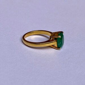 May include: A gold ring with a large, oval-shaped emerald gemstone.