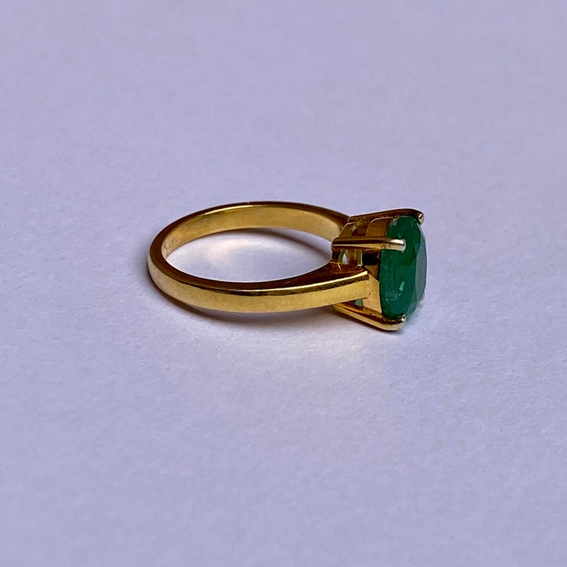 May include: A gold ring with a large, oval-shaped emerald gemstone.