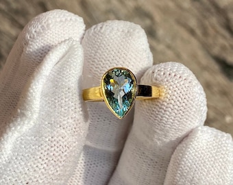 May include: A pear-shaped aquamarine gemstone set in a gold ring. The ring is simple and elegant, with a smooth band and a delicate setting for the stone.