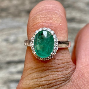 May include: A silver ring with a large oval emerald gemstone surrounded by a halo of smaller diamonds.
